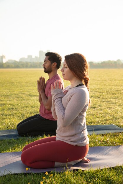 Vista lateral de um homem e uma mulher meditando ao ar livre em esteiras de ioga