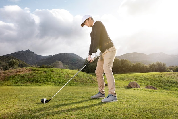 Vista lateral de um homem jogando golfe no campo com o taco