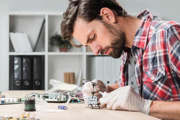 Vista lateral, de, um, homem jovem, reparar, helicóptero, brinquedo, sobre, escrivaninha madeira