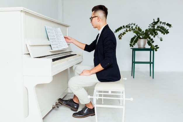 Vista lateral, de, um, homem jovem, sentando, frente, piano, leitura, a, musical, folha