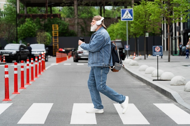 Foto grátis vista lateral de um homem mais velho atravessando a rua enquanto ouve música em fones de ouvido