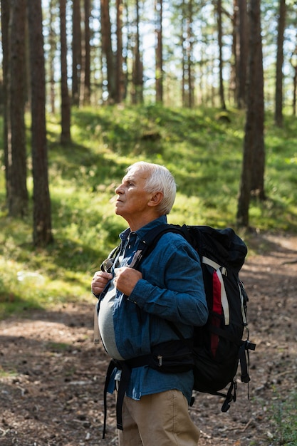 Vista lateral de um homem mais velho viajando com uma mochila na natureza