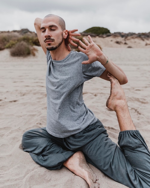 Vista lateral de um homem na praia fazendo ioga