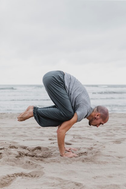 Vista lateral de um homem na praia praticando ioga