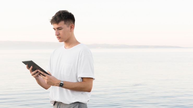 Foto grátis vista lateral de um homem na praia segurando um tablet com espaço de cópia