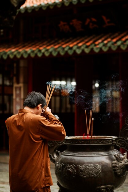 Vista lateral de um homem religioso no templo queimando incenso e copiando espaço