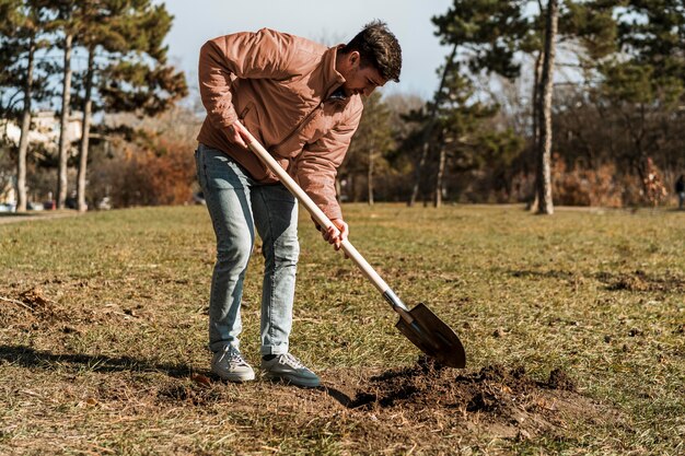 Vista lateral de um homem usando uma pá para cavar um buraco para plantar uma árvore
