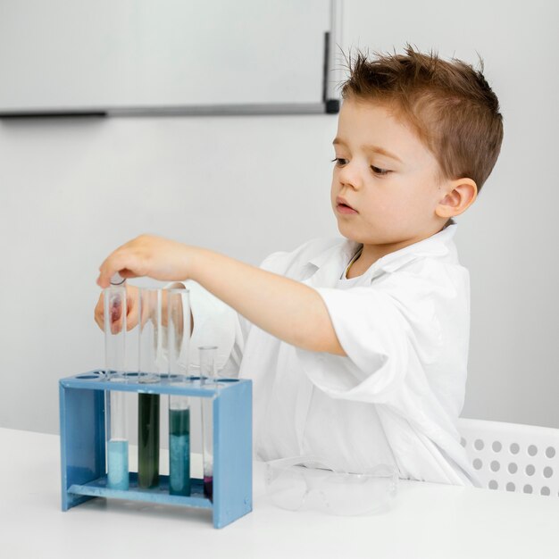 Foto grátis vista lateral de um menino cientista no laboratório fazendo experiências com tubos de ensaio