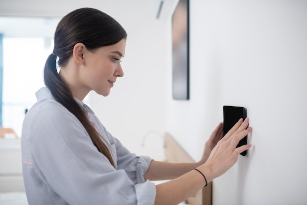 Vista lateral de uma bela jovem concentrada em prender o tablet na parede