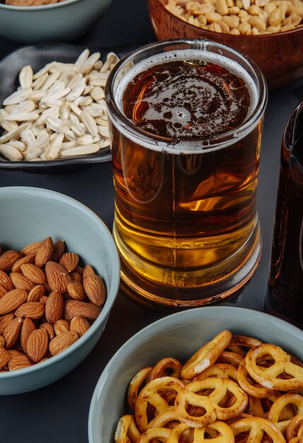 Vista lateral de uma caneca de cerveja com snacks amendoins sementes de girassol amêndoa e mini pretzels em preto