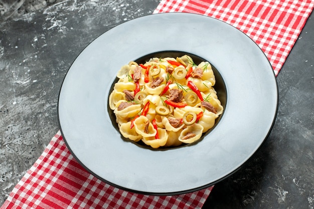 Vista lateral de uma deliciosa conchiglie com legumes em um prato e uma faca em uma toalha vermelha despojada sobre fundo cinza