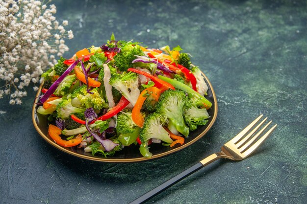 Vista lateral de uma deliciosa salada vegana em um prato com vários vegetais e garfo de flor branca em fundo escuro