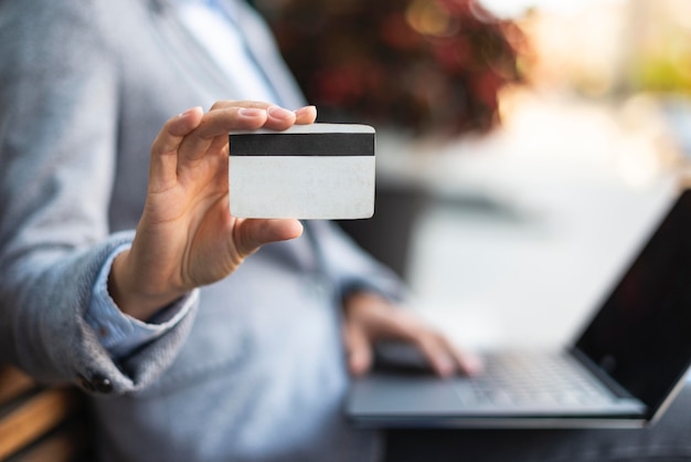 Vista lateral de uma empresária segurando um cartão de crédito enquanto usa o laptop