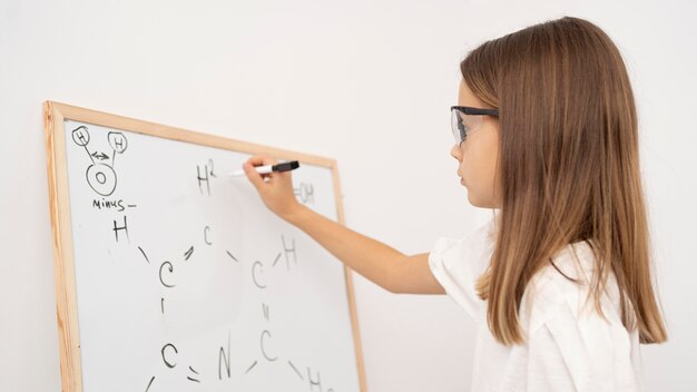 Vista lateral de uma garota aprendendo ciências com o quadro branco