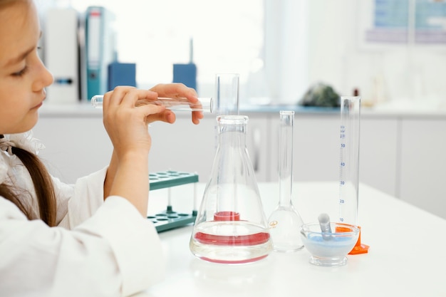 Vista lateral de uma garota cientista no laboratório com tubos de ensaio fazendo experiências