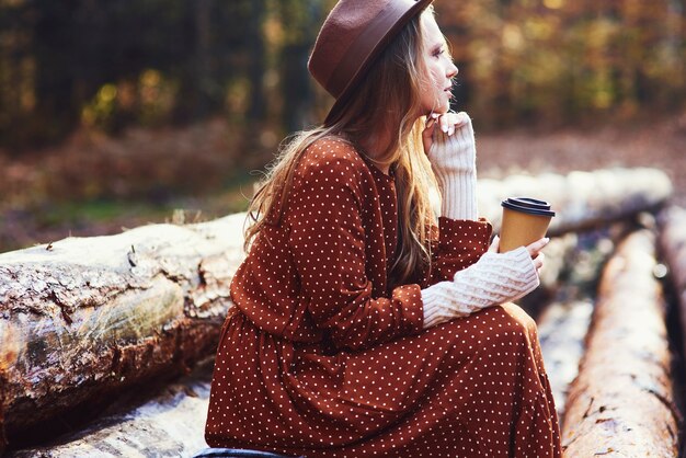 Vista lateral de uma linda mulher tomando café na floresta de outono