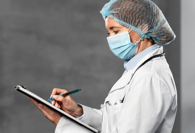Vista lateral de uma médica com máscara médica e rede para cabelo segurando a prancheta com espaço de cópia