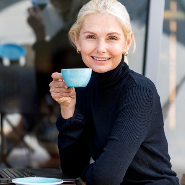 Vista lateral de uma mulher de negócios mais velha tomando café ao ar livre enquanto trabalha
