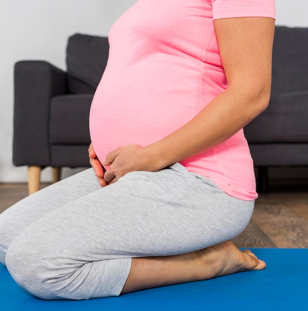 Vista lateral de uma mulher grávida em casa na esteira de ginástica