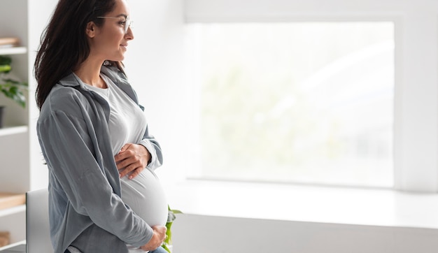 Vista lateral de uma mulher grávida segurando a barriga em casa com espaço de cópia