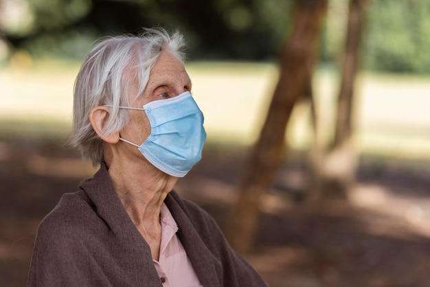 Vista lateral de uma mulher idosa com máscara médica ao ar livre e copie o espaço