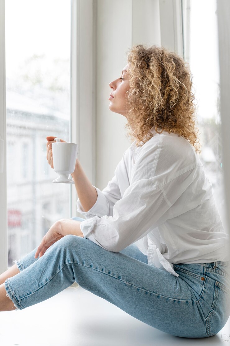 Foto grátis vista lateral de uma mulher loira de cabelos cacheados relaxando em casa com uma xícara de café