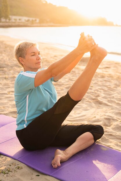 Vista lateral de uma mulher mais velha fazendo ioga na praia
