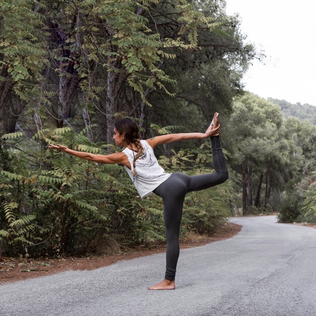Vista lateral de uma mulher na estrada fazendo ioga