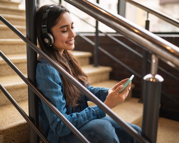 Foto grátis vista lateral de uma mulher ouvindo música no fone de ouvido enquanto está sentada na escada