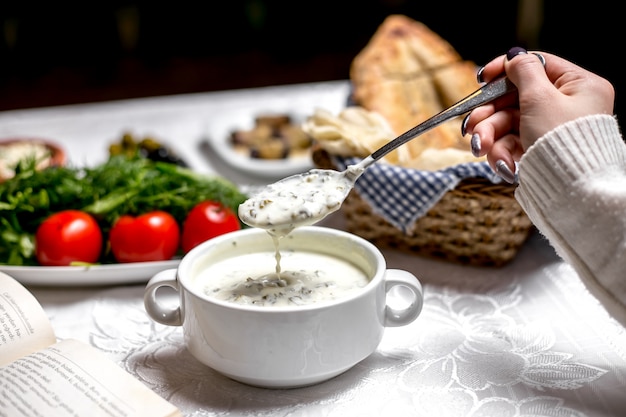 Vista lateral de uma mulher que come uma sopa tradicional dovga-iogurte de prato azerbaijano com legumes e ervas