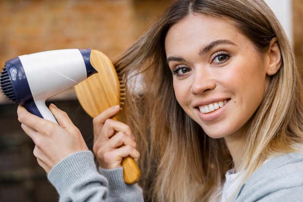 Vista lateral de uma mulher secando o cabelo com uma escova