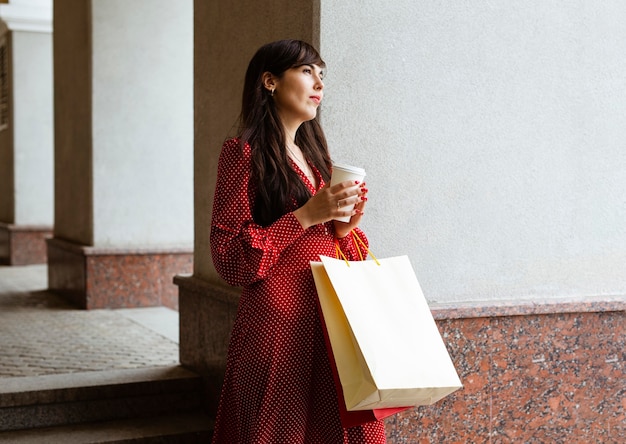 Vista lateral de uma mulher segurando uma xícara de café e sacolas de compras