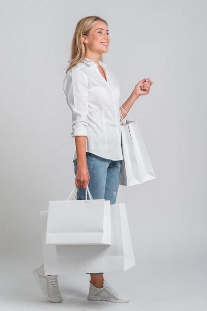 Vista lateral de uma mulher sorridente segurando várias sacolas de compras