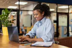 Foto grátis vista lateral de uma mulher sorridente trabalhando com um laptop no escritório
