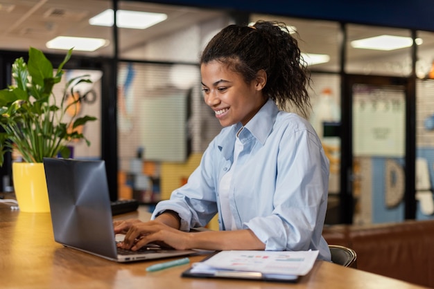 Vista lateral de uma mulher sorridente trabalhando com um laptop no escritório