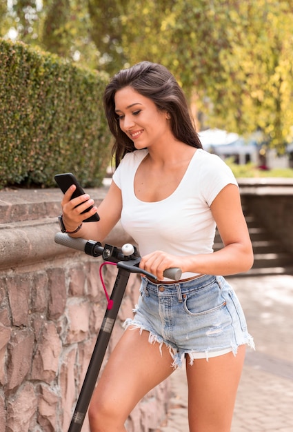 Vista lateral de uma mulher verificando seu smartphone enquanto está na scooter elétrica