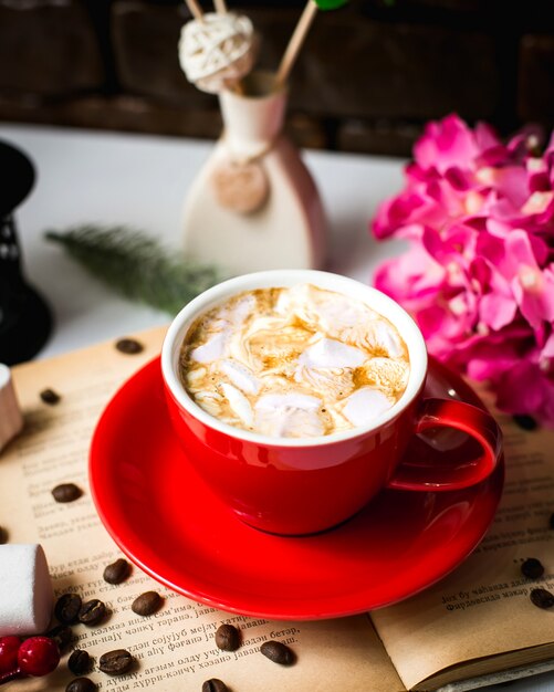 Vista lateral de uma xícara de café com marshmallows e grãos de café na mesa