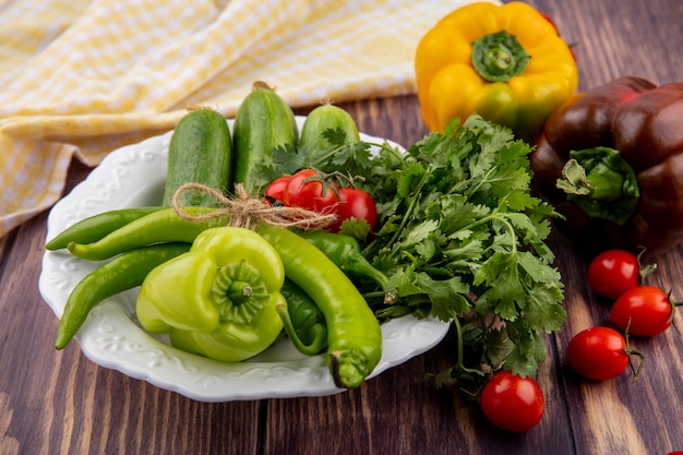 Vista lateral de vegetais como pimenta, coentro pepino no prato e pano xadrez com tomates na madeira