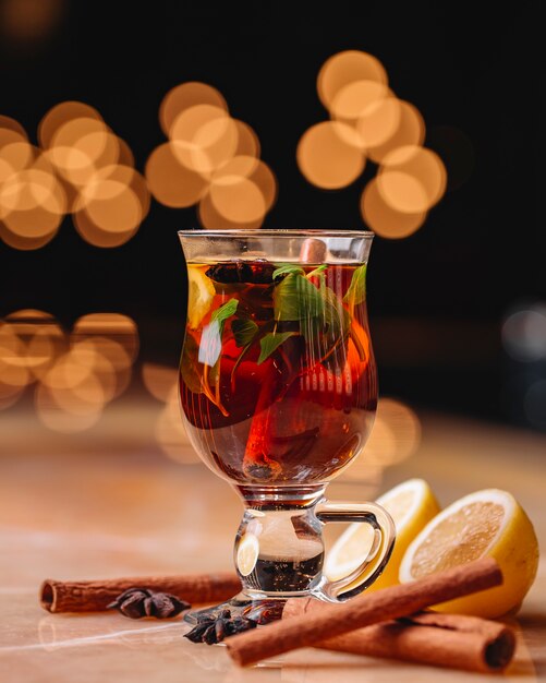 Vista lateral de vinho quente com anis de canela e laranja em um copo na mesa em fundo escuro