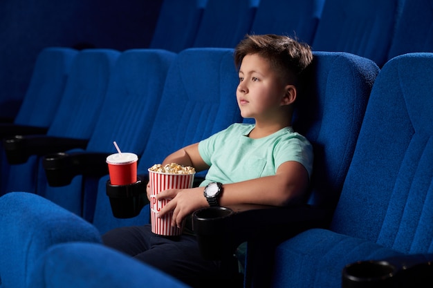 Vista lateral do adolescente masculino relaxado comendo comida lixo no cinema