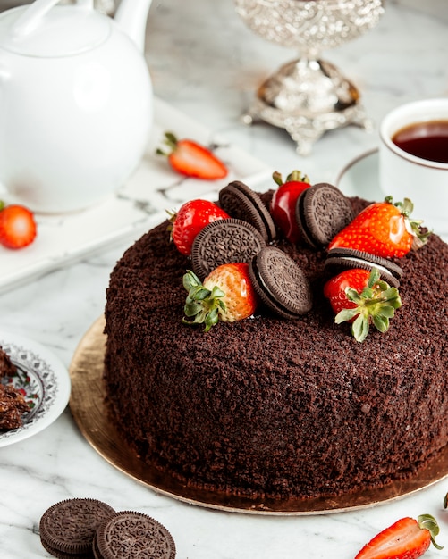 Vista lateral do bolo de chocolate decorado com morangos e biscoitos em cima da mesa