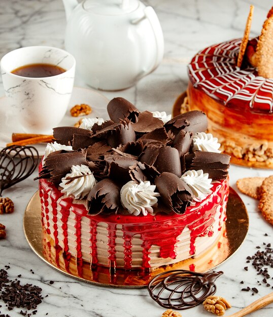 Vista lateral do bolo de frutas coberto com raspas de chocolate e chantilly em cima da mesa, servida com chá