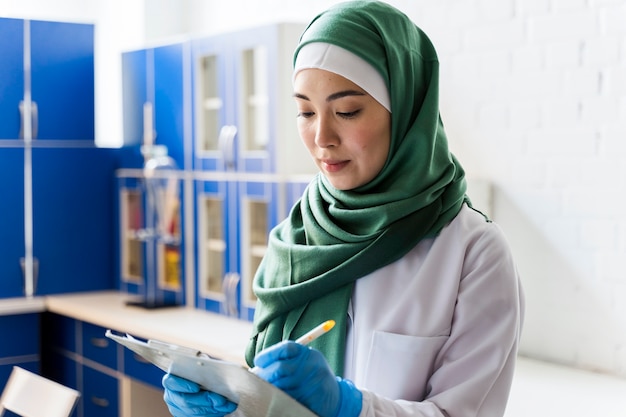 Vista lateral do cientista feminina com hijab e bloco de notas