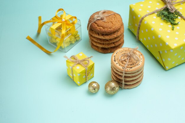 Vista lateral do clima de Natal com vários biscoitos deliciosos empilhados e uma linda caixa de presente amarela ao lado do acessório de decoração no lado direito sobre fundo verde pastel