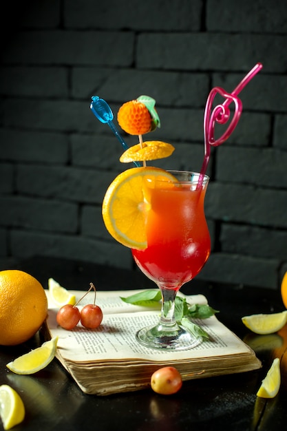 Vista lateral do cocktail exótico com fatia de limão e palha em um copo no escuro