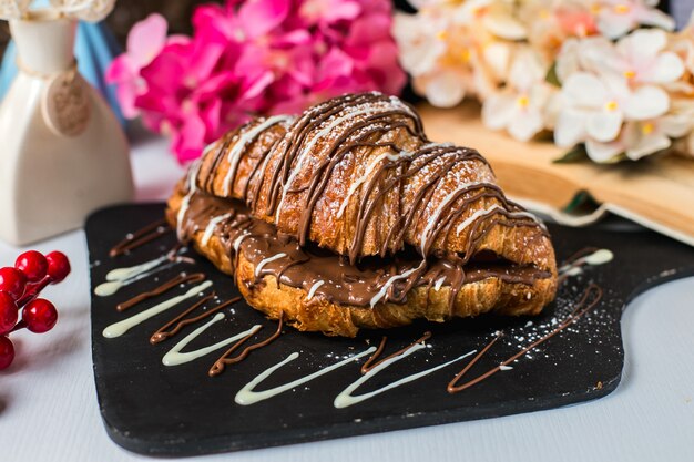 Vista lateral do croissant decorado com chocolate em uma placa de madeira