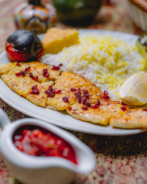 Foto grátis vista lateral do filé de peixe assado, decorado com bérberis, guarnecido com arroz e tomate grelhado em um prato branco