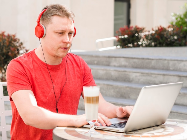 Vista lateral do homem com café com leite e trabalhando no laptop