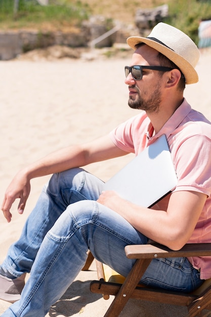 Vista lateral do homem com o laptop na praia