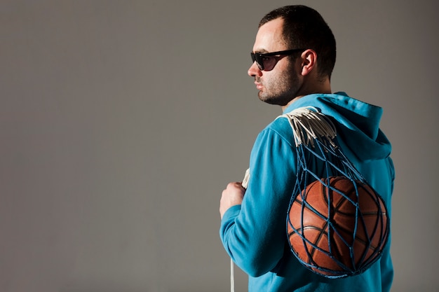 Foto grátis vista lateral do homem de capuz segurando basquete na rede com espaço de cópia